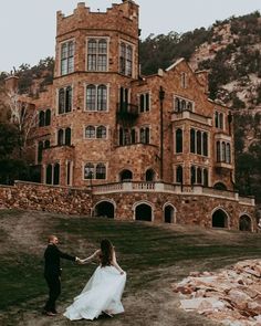 a bride and groom holding hands in front of an old castle like building on a hill