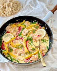 a skillet filled with shrimp and vegetables on top of a white cloth next to a wooden spoon