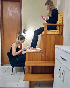 a woman sitting in a chair looking at her cell phone while another sits on the floor