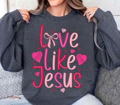 a woman wearing a sweatshirt with the words love like jesus printed in pink on it