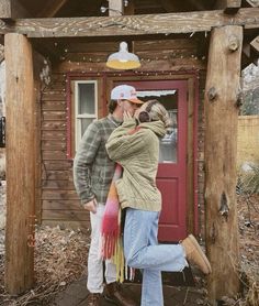 a man and woman kissing in front of a small cabin with a red door on the side