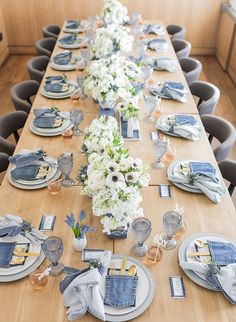 a long wooden table with blue and white plates, napkins and flowers on it