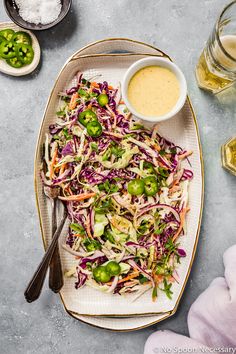 a white plate topped with coleslaw slaw next to two bowls of dressing