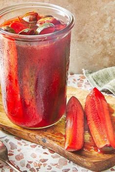 a jar filled with liquid sitting on top of a cutting board next to sliced strawberries