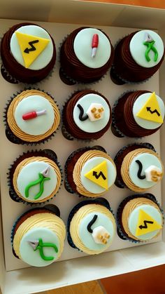 twelve cupcakes in a box decorated with different designs and shapes, including the letter j