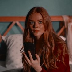 a woman with long red hair holding a cell phone in her hand and looking at the screen