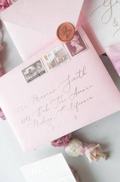 a pink envelope with a wax stamp on it next to some flowers and other items