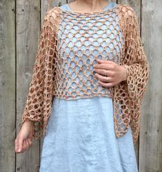 a woman standing in front of a wooden fence wearing a blue dress and brown cardigan