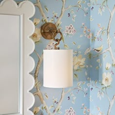 a lamp on a wall next to a mirror and flowered wall paper with scalloped edges