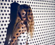 a woman with long hair standing in front of a wall covered in polka dotes