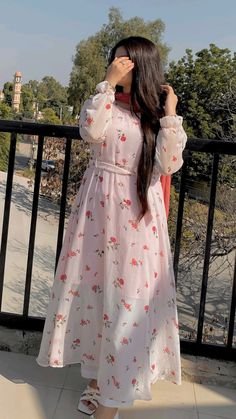 a woman in a dress standing on a balcony looking at the sky with her hands to her face