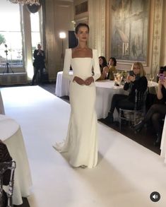 a woman in a white dress is walking down the runway at a fashion show with other people