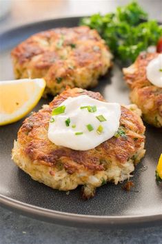 crab cakes with sour cream and lemon wedges on a black plate, garnished with parsley