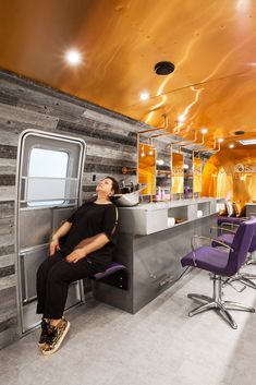 a woman sitting on a chair in front of a counter with purple chairs and lights