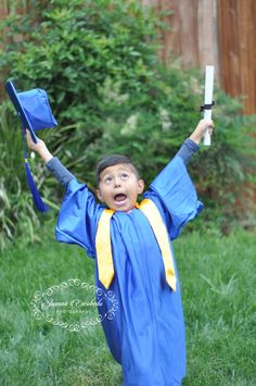 a young boy wearing a graduation gown and holding his arms in the air