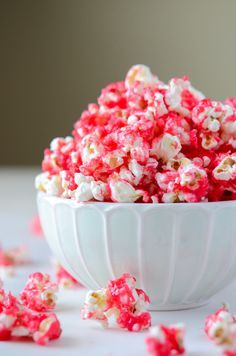 a white bowl filled with red and white popcorn on top of a table next to scattered candy