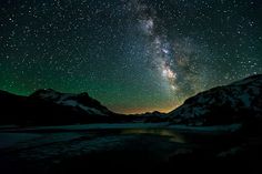 the night sky is filled with stars above mountains and snow - capped peaks, as seen from an icy lake