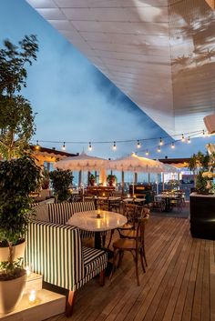 an outdoor dining area with tables and umbrellas over looking the ocean at night time