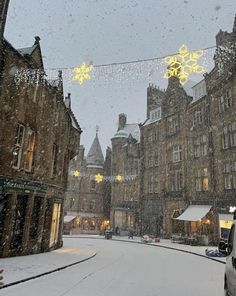 a snowy street with cars parked on the side and buildings in the background, all lit up by christmas lights