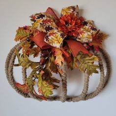 a wreath made out of rope with autumn leaves and bows on the front, hanging on a wall