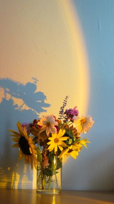 a vase filled with yellow and purple flowers on top of a wooden table next to a rainbow