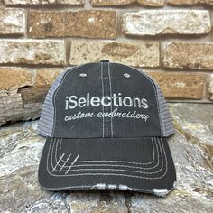 a black and gray hat with the words selections written on it, sitting against a brick wall