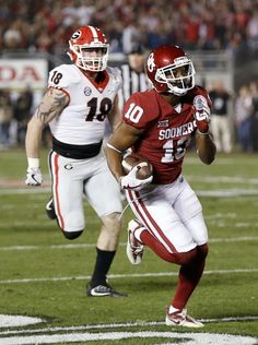 a football player running with the ball in his hand and another person behind him on the field