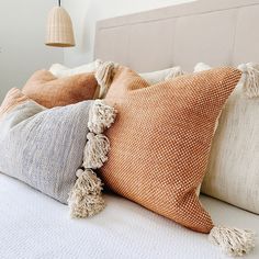 four different colored pillows on a bed with a lamp in the background and a white headboard