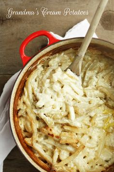 a red pot filled with pasta and cheese on top of a white napkin next to a wooden table