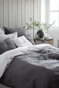 an unmade bed with grey sheets and pillows