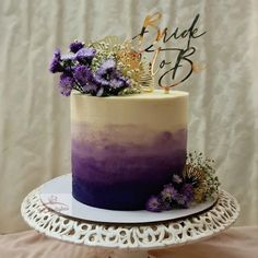 a purple and white ombreed cake with flowers on top sits on a table