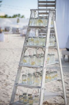 an old ladder is filled with mason jars and lemonade glasses on the sand at a beach