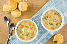 two bowls of soup on a wooden table with bread and oranges next to it