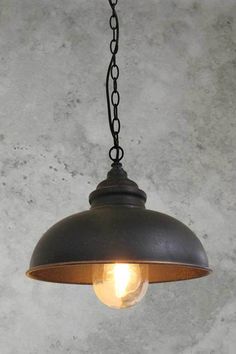 an old fashioned light hanging from a chain on the ceiling in a room with concrete walls