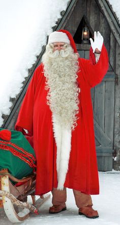 a man dressed as santa claus standing in front of a sleigh with his hand up