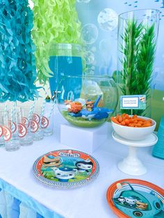 a table topped with plates filled with food next to vases and fishbowes