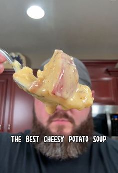 a man is holding up a piece of cheesey potato soup with a spoon in his hand