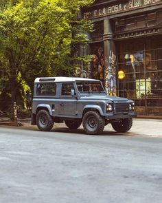 a gray jeep parked in front of a building on the side of a street next to trees