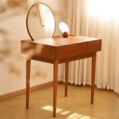 a mirror sitting on top of a wooden table in front of a window next to a white curtain