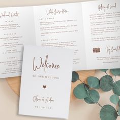 wedding program booklets with eucalyptus leaves and greenery on the table next to it