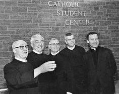 a group of men standing next to each other in front of a brick wall with the words catholic student center on it