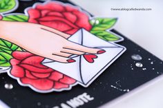 a hand holding an envelope with roses on it and the words love is in the air