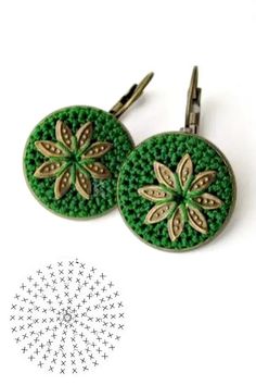 two green and gold earrings sitting on top of a white table next to a pair of scissors