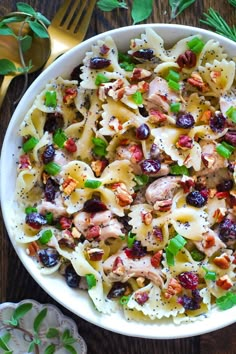 a pasta salad with chicken, olives and cranberries in a white bowl