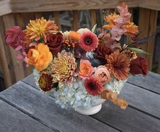 a vase filled with lots of different colored flowers on top of a wooden table next to a fence