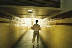 a man walking down a long hallway with yellow tiles on the walls and flooring