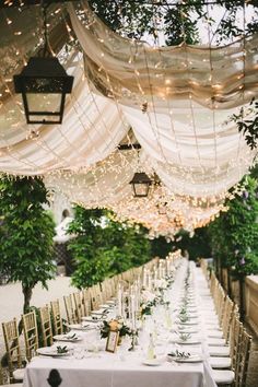 a long table is set with white linens and greenery for an outdoor wedding reception