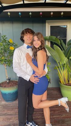 a young man and woman posing for a photo in front of some potted plants