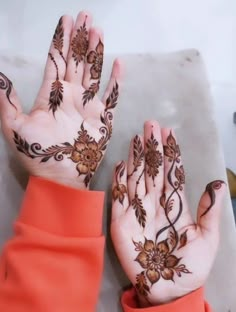 two hands with henna designs on them, one is orange and the other is brown