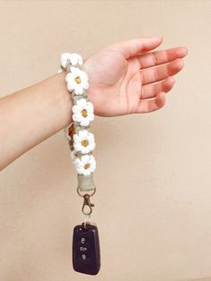 a woman's hand holding a bracelet with flowers and a car key on it